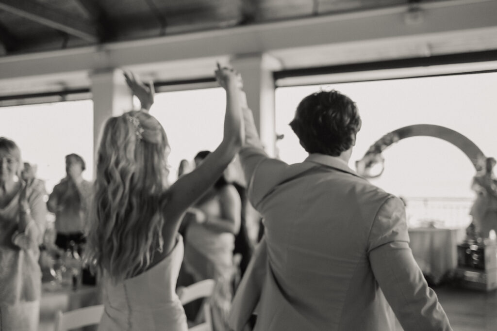 Bride and groom dancing at their reception under a covered deck with guests around them.