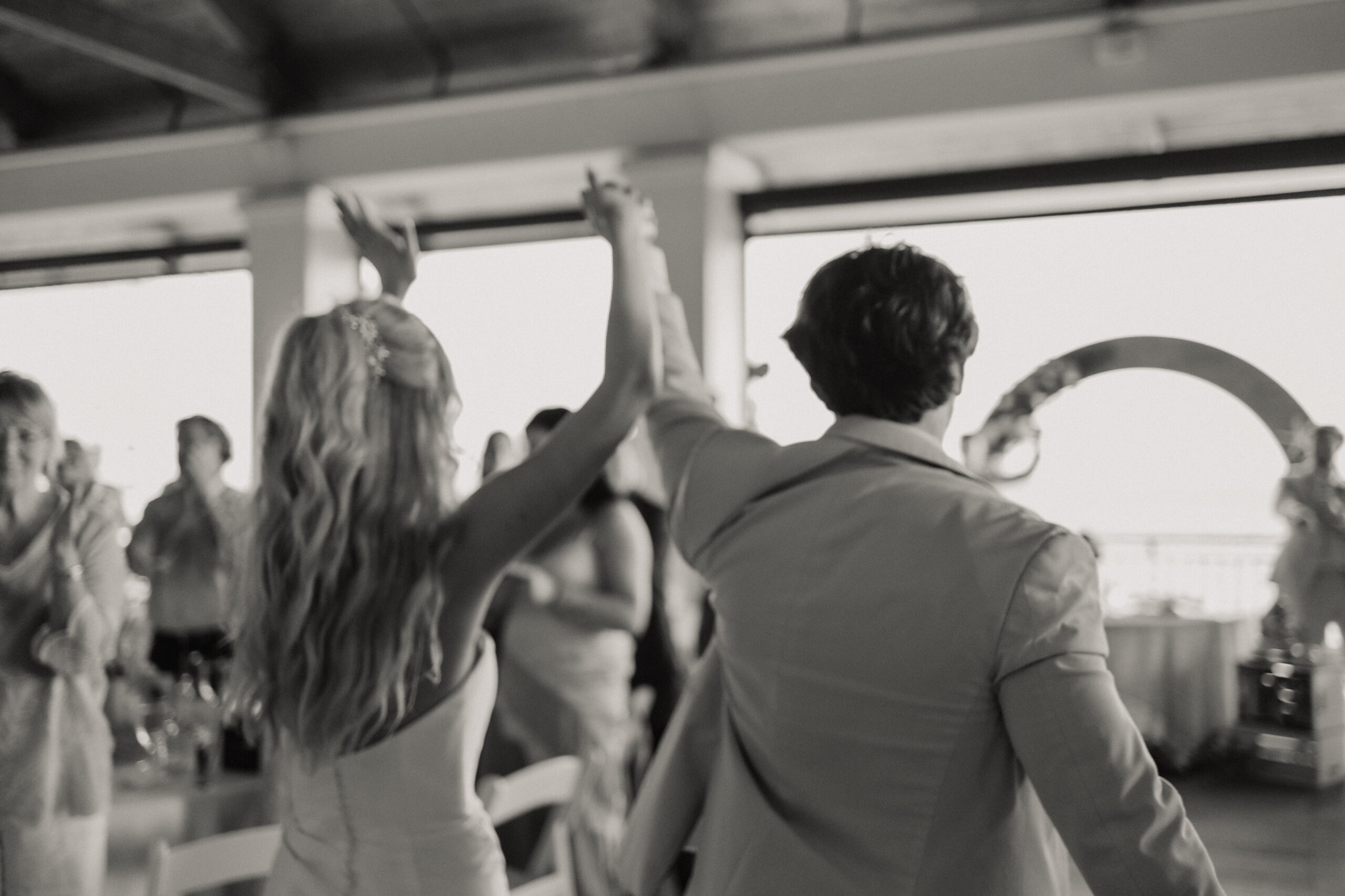 Bride and groom dancing at their reception under a covered deck with guests around them.