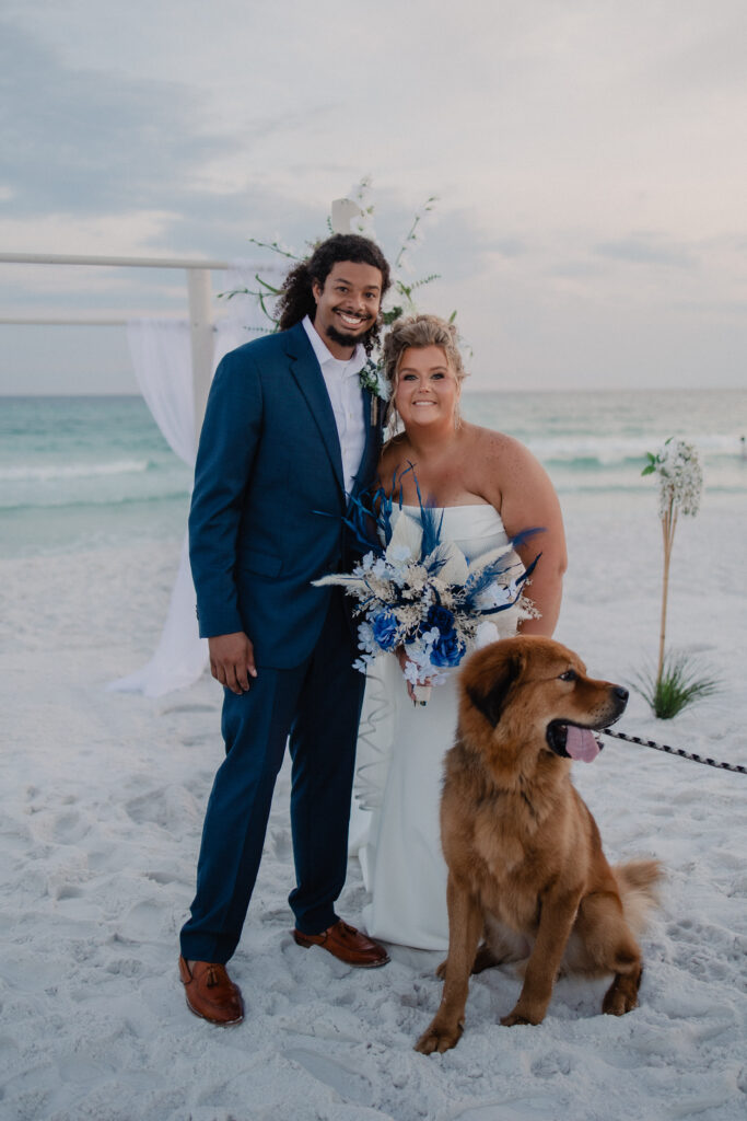 Newlywed couple with their dog pose at a beachfront wedding ceremony on 30A, Florida, with the emerald waters of the Gulf behind them.