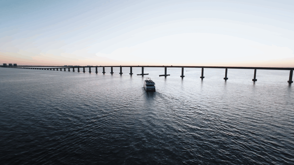 Boat sails under the Destin bridge at sunset on Florida’s Emerald Coast, creating a cinematic backdrop for a Gulf Coast wedding film.