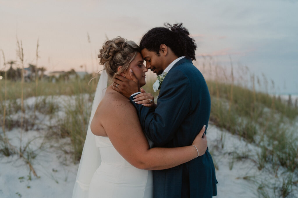 Bride and groom embracing on a Gulf Coast beach during a backlit golden-hour portrait with warm sunset light glowing around them.