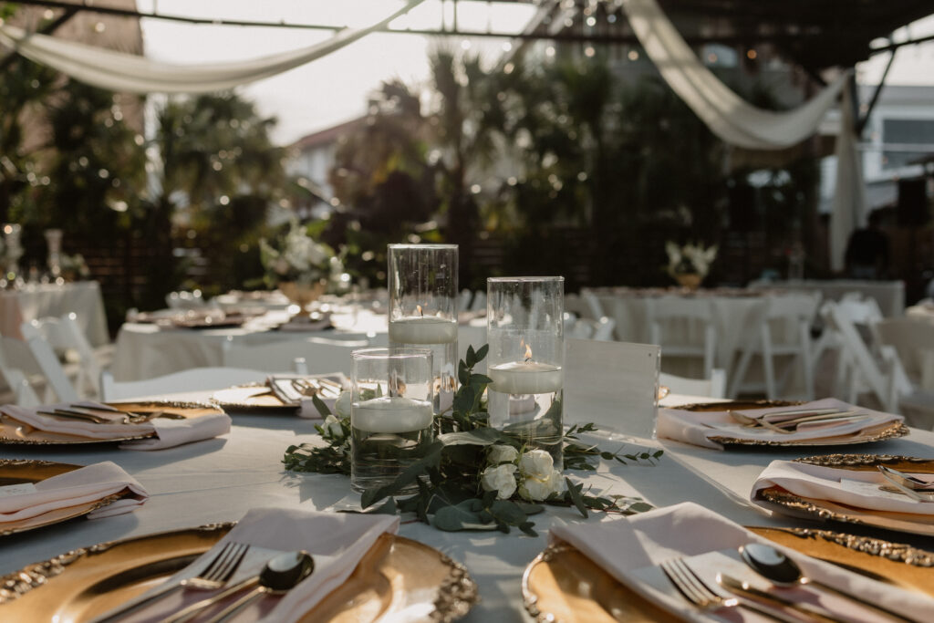 Elegant wedding reception table set with white florals, taper candles, and fine china under a crystal chandelier at a Gulf Coast luxury venue.